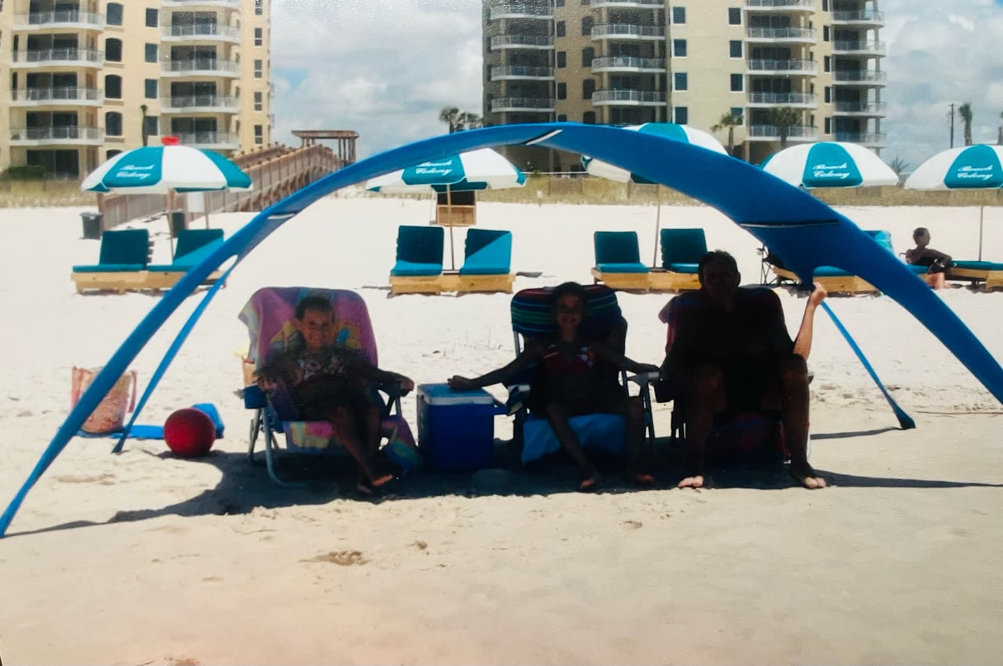 Archival photograph of three family members seated under an early Shady Baby prototype canopy on the beach